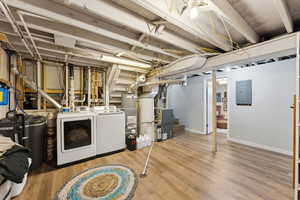 Basement featuring independent washer and dryer, electric panel, gas water heater, baseboards, and wood finished floors