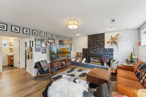 Living area featuring light wood-style flooring, a brick fireplace, baseboards, and brick wall