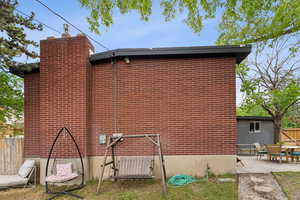 View of side of home with fence, a patio, brick siding, and a chimney