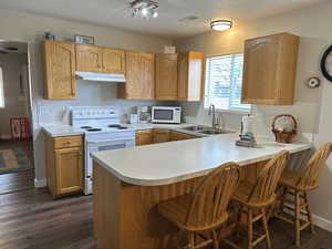 Kitchen featuring white appliances, under cabinet range hood, a sink, light countertops, and a textured ceiling