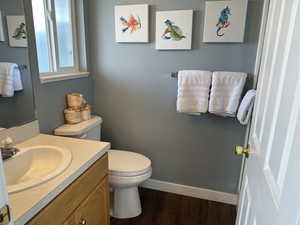 Half bathroom with wood finished floors, vanity, toilet, and baseboards