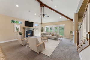 Living area featuring beam ceiling, a glass covered fireplace, stairs, ceiling fan, and plenty of natural light