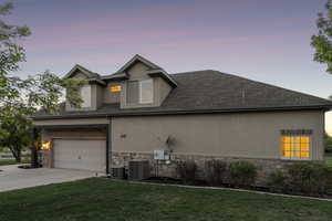 View of side of home with stucco siding, stone siding, driveway, central AC unit, and a yard