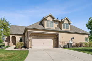 View of front facade featuring stucco siding, stone siding, driveway, and a front lawn