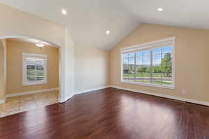 Empty room with arched walkways, plenty of natural light, wood finished floors, vaulted ceiling, and recessed lighting