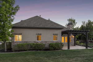Back of property with stone siding, a pergola, stucco siding, a lawn, and a shingled roof