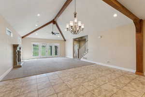 Unfurnished living room featuring beamed ceiling, light carpet, stairs, a chandelier, and ceiling fan