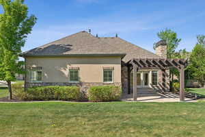 Back of house with a pergola, stone siding, stucco siding, and a yard