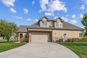 Traditional-style home featuring stucco siding, stone siding, driveway, and a front lawn