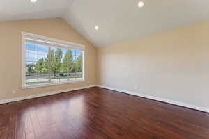 Spare room featuring lofted ceiling, dark wood finished floors, baseboards, and recessed lighting