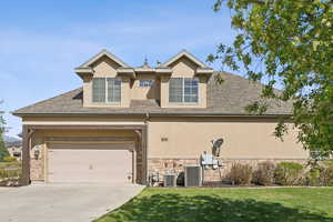View of front of home featuring stucco siding, driveway, stone siding, cooling unit, and a front lawn