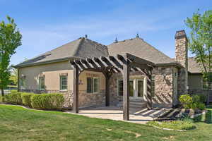 Back of house with a pergola, stone siding, and a yard