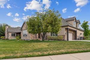 View of front of property with stucco siding, stone siding, concrete driveway, a front lawn, and a garage