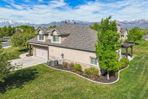 View of side of home with stucco siding, stone siding, concrete driveway, a mountain view, and a yard