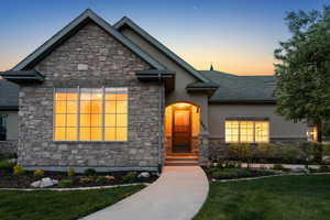 View of front of property featuring stone siding, stucco siding, a yard, and a shingled roof