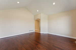 Empty room with arched walkways, recessed lighting, baseboards, dark wood finished floors, and vaulted ceiling