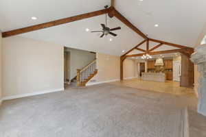 Unfurnished living room with beam ceiling, a ceiling fan, a chandelier, stairs, and baseboards