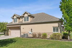 View of property exterior featuring stucco siding, stone siding, concrete driveway, and a yard