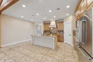 Kitchen featuring appliances with stainless steel finishes, premium range hood, arched walkways, a sink, and tasteful backsplash