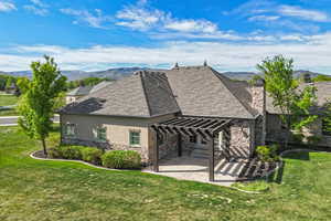 Rear view of property featuring stone siding, stucco siding, a pergola, a patio area, and a yard