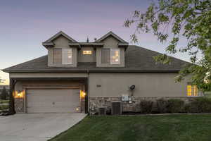 View of front of house with stucco siding, concrete driveway, central AC, and stone siding