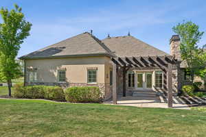 Back of house with stone siding, a pergola, stucco siding, and a patio