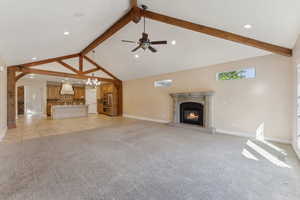 Unfurnished living room featuring beamed ceiling, a glass covered fireplace, baseboards, light carpet, and high vaulted ceiling