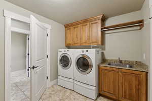Clothes washing area featuring washer and clothes dryer, cabinet space, and baseboards