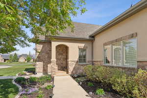 Doorway to property with stone siding, stucco siding, a lawn, and a shingled roof