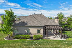 Back of house with stucco siding, stone siding, a pergola, a lawn, and a patio