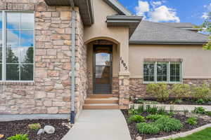 View of exterior entry featuring stucco siding, stone siding, and roof with shingles