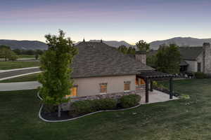 Property exterior at dusk featuring stucco siding, a pergola, a chimney, a patio, and a lawn