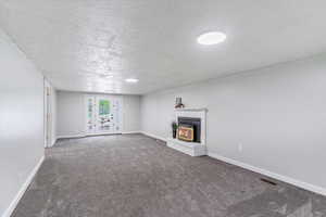 Unfurnished living room with carpet, baseboards, a textured ceiling, and a fireplace
