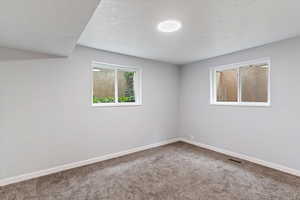 Carpeted empty room with a textured ceiling and baseboards