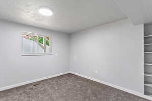 Spare room featuring a textured ceiling, carpet floors, and baseboards