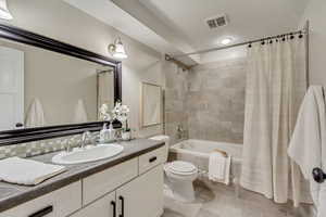 Bathroom with tiled shower / bath combo, toilet, vanity, and tile patterned flooring