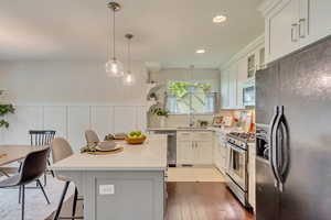 Kitchen with appliances with stainless steel finishes, a sink, hardwood / wood-style floors, light countertops, and a kitchen breakfast bar