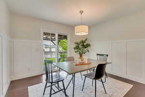 Dining room featuring a decorative wall, a wainscoted wall, and dark wood-type flooring