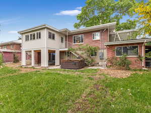 Back of house featuring a hot tub, a lawn, a patio area, and brick siding