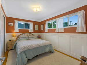 Bedroom featuring wainscoting, crown molding, wood finished floors, and a decorative wall