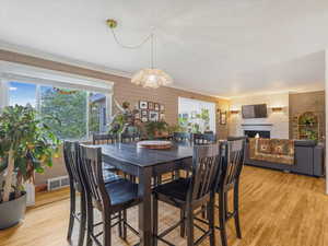 Dining space with brick wall, light wood-style floors, a fireplace, and crown molding