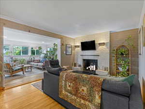 Living area featuring a large fireplace, wood finished floors, crown molding, and brick wall