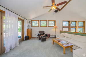 Carpeted living room with baseboard heating, vaulted ceiling, and ceiling fan