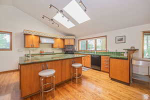 Kitchen with appliances with stainless steel finishes, a skylight, vaulted ceiling, wall chimney exhaust hood, and a sink