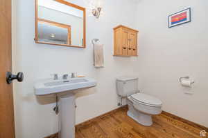 Half bathroom featuring wood finished floors, toilet, and baseboards