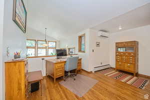 Home office featuring baseboard heating, light wood-type flooring, a wall mounted AC, baseboards, and lofted ceiling