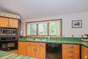 Kitchen featuring black appliances, a sink, tasteful backsplash, tile countertops, and brown cabinets
