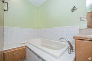 Full bathroom featuring a bath, vanity, tile walls, and vaulted ceiling