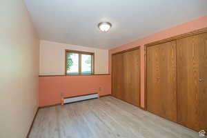 Unfurnished bedroom with a baseboard heating unit, light wood-style floors, multiple closets, and baseboards