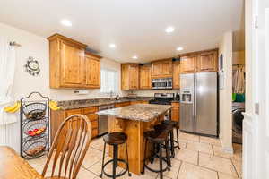 Kitchen featuring appliances with stainless steel finishes, a sink, washer / clothes dryer, light tile patterned floors, and brown cabinetry